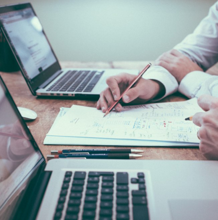 Männer arbeiten an Zetteln zwischen zwei Laptops