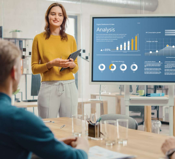 Frau steht neben einem Bildschirm, auf dem eine Präsentation läuft